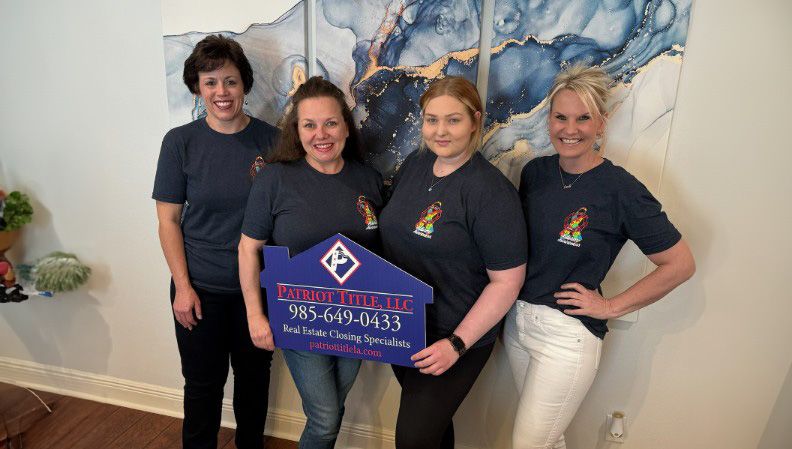 Four Patriot Title team members holding a Patriot Title, LLC Real Estate Closing Specialists sign